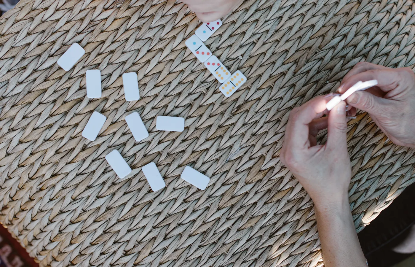 Manos jugando una partida de dominó sobre una mesa tejida